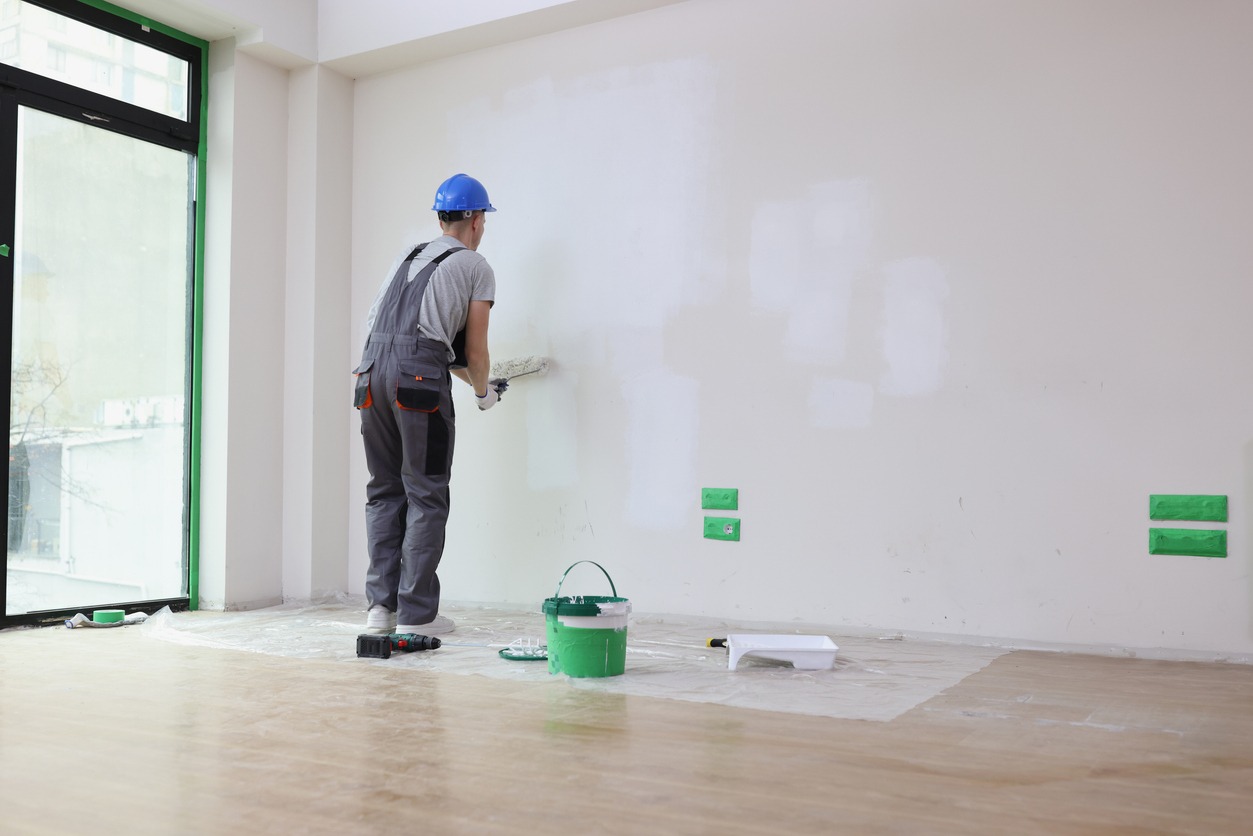 Foreman paints wall in white with roller dipped in bucket