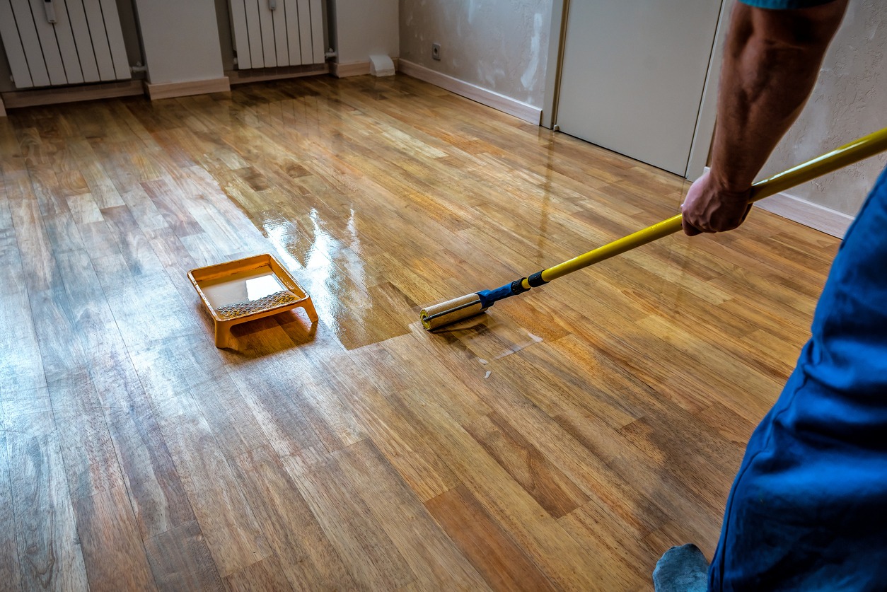 Parquet floor renovation. Lacquering wood floors. Worker uses a roller to coating floors