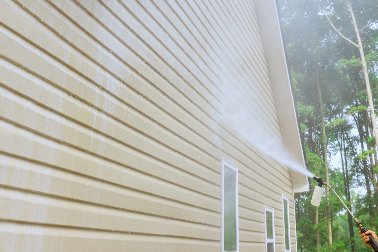 Service worker utilizes high pressure nozzles to efficiently clean siding houses with a water soap cleaner.