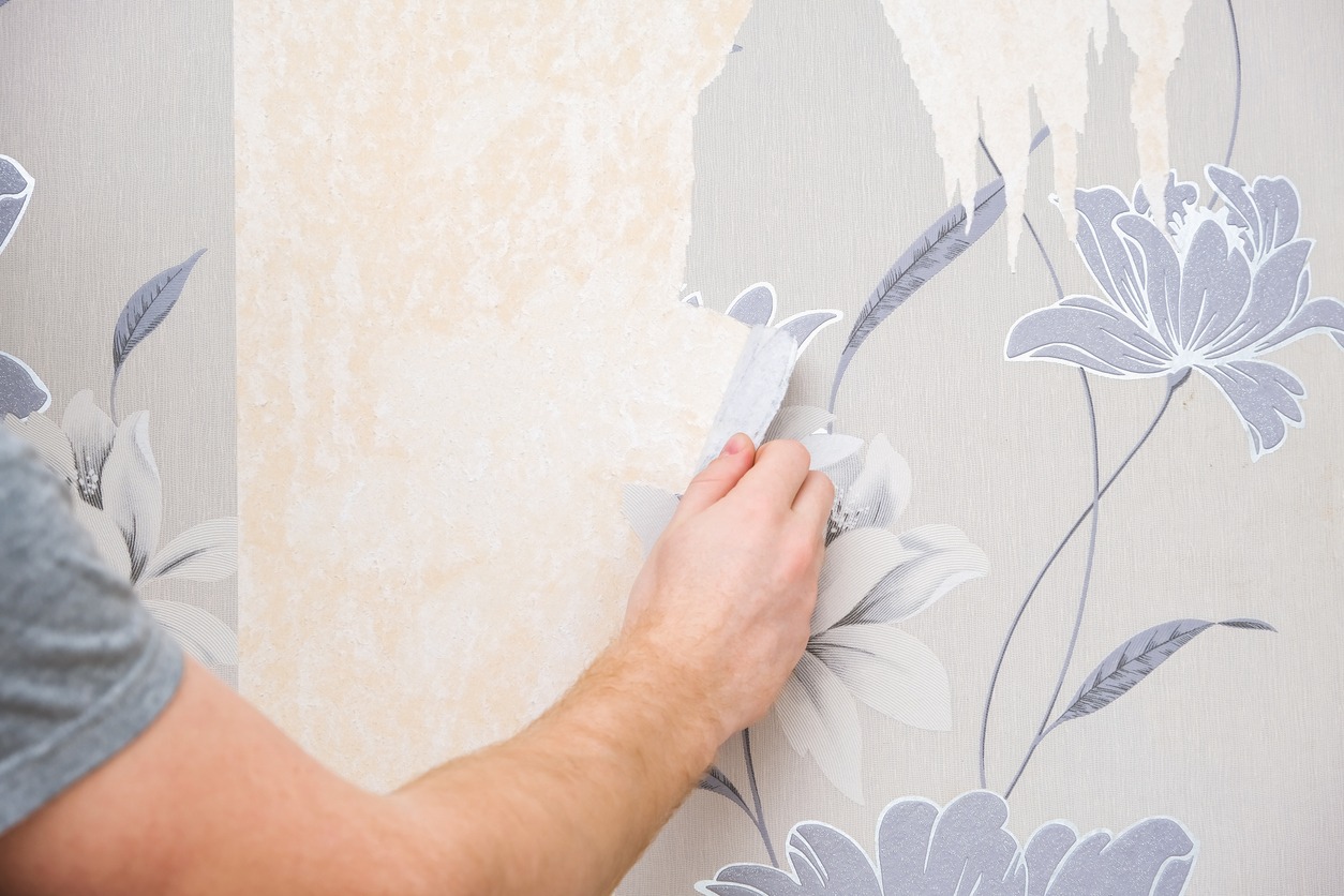 Removing old wallpaper with a spatula and a sprayer with water. A man removes old wallpaper in room.