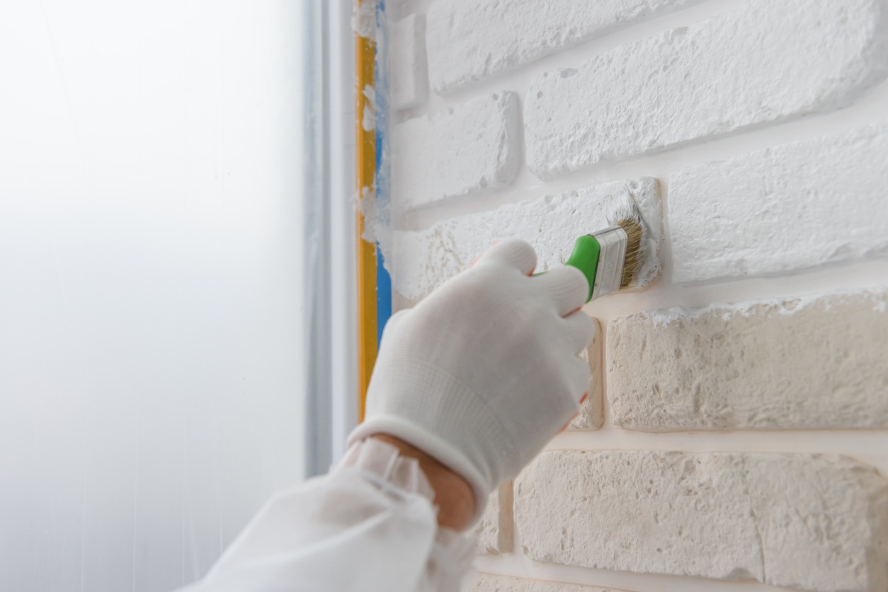 Worker is painting a brick wall with a brush