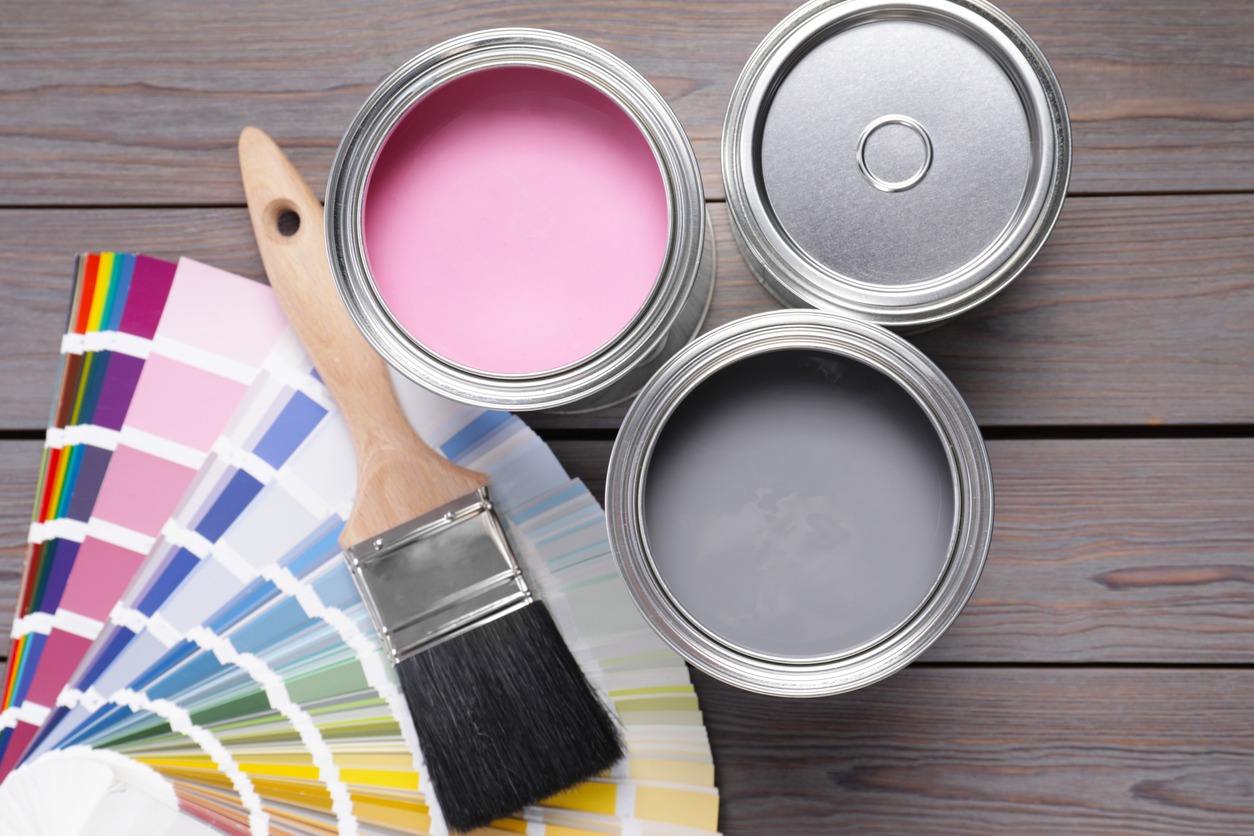 Cans of pink and grey paints, palette with brush on wooden table, flat lay