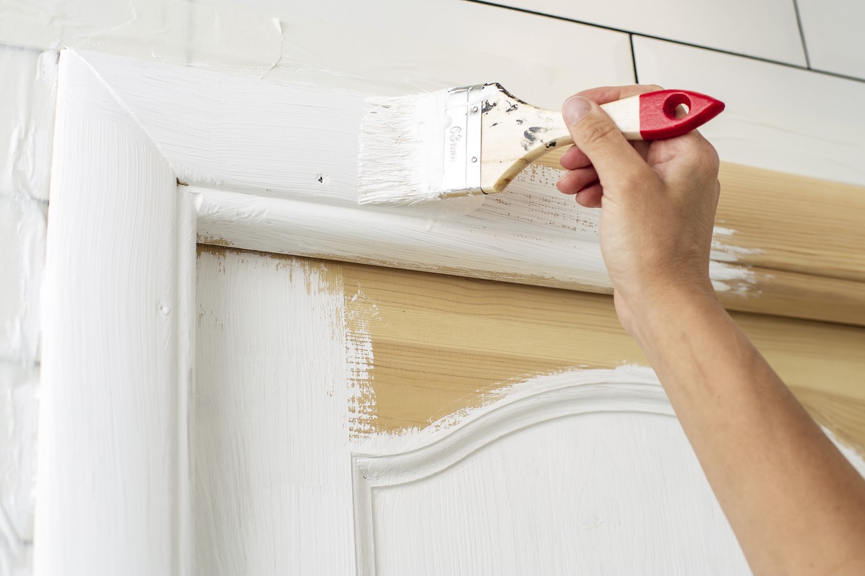 Hand with a brush paints a wooden door frame