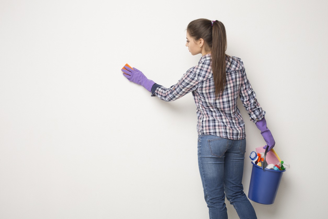 Young woman wiping white wall