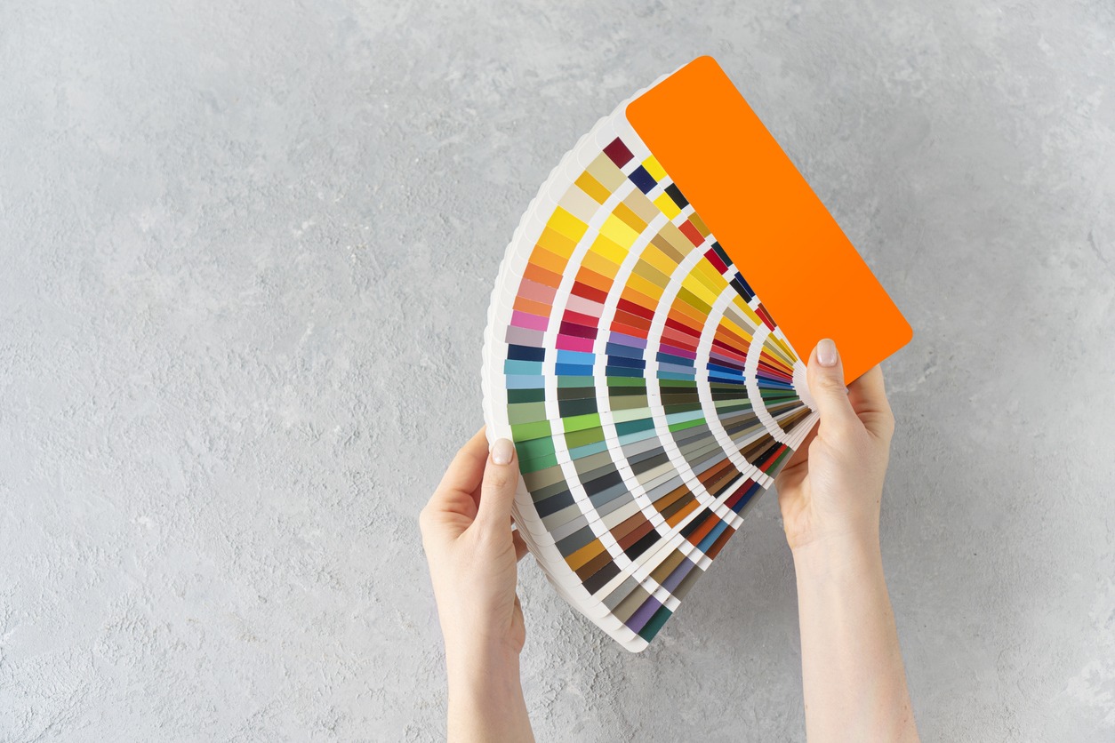 What color to paint the walls concept. Female hands holding a ral colors palette fan on a concrete background. Copy space.