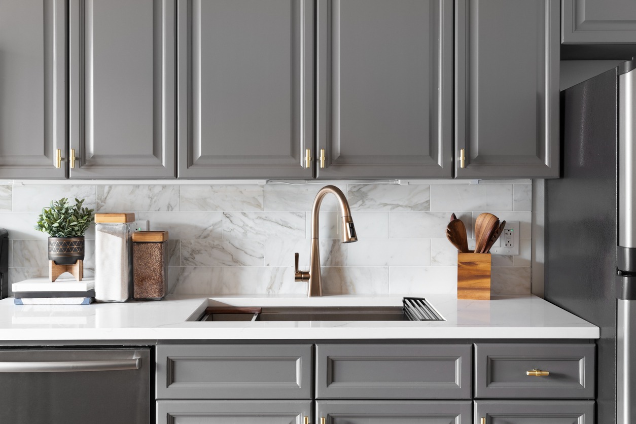 A gold kitchen faucet detail with grey cabinets.