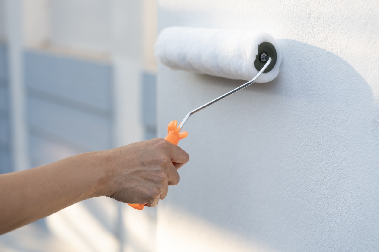 Hand worker holding brush painting roller white on the wall house