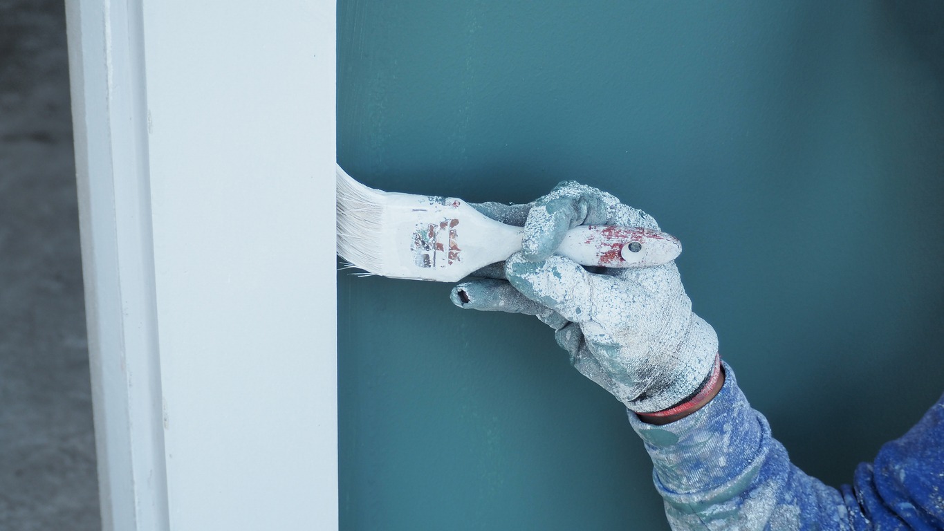 A worker is painting the walls of the house with a primer using a paint roller.