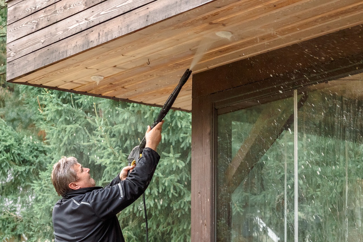 Man cleaning walls and floor with high pressure power washer. Washing terrace wood planks and cladding walls.