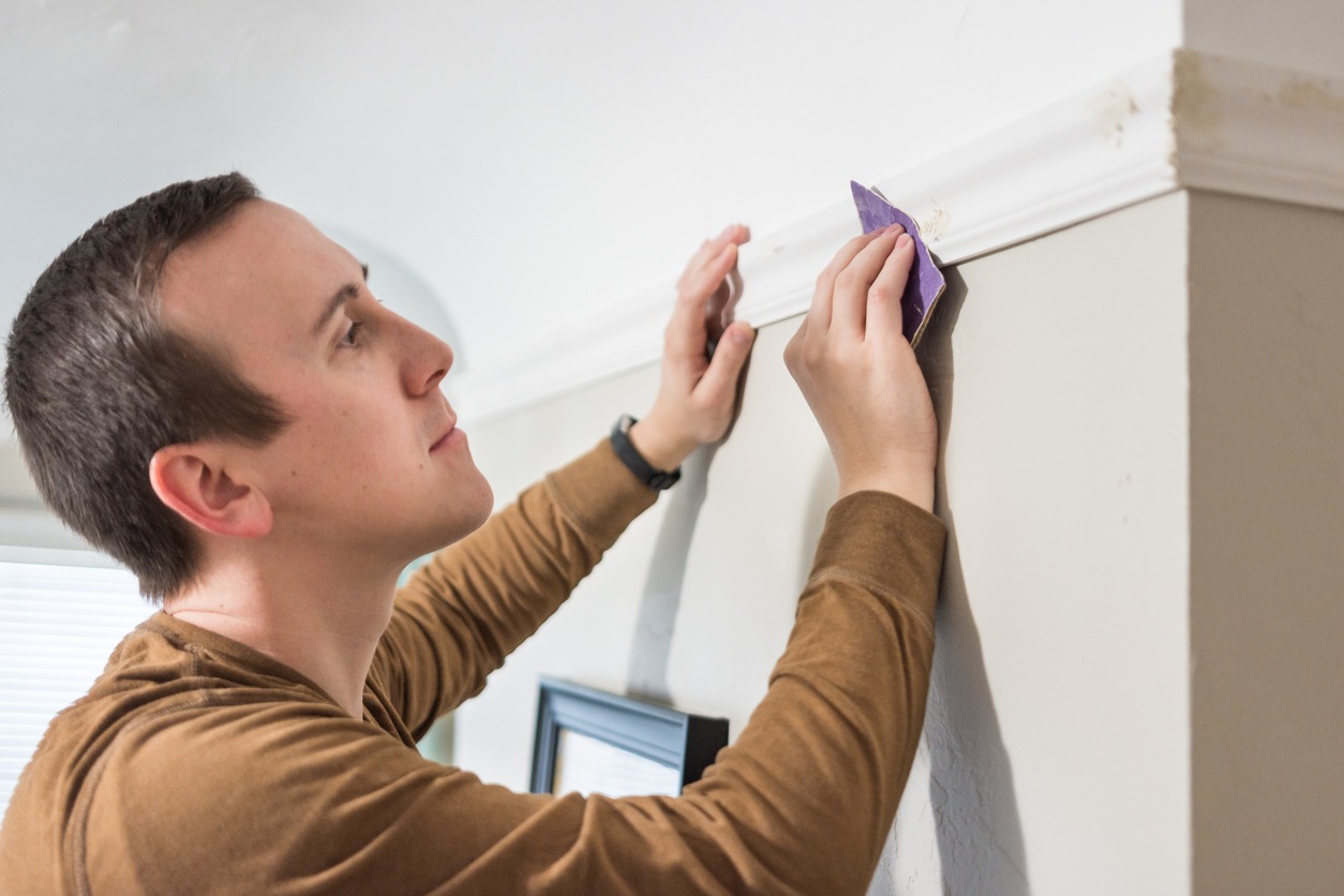 Young man sanding nail holes on white trim board