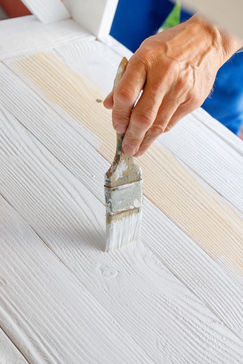 Worker painting white wooden furniture outdoor.