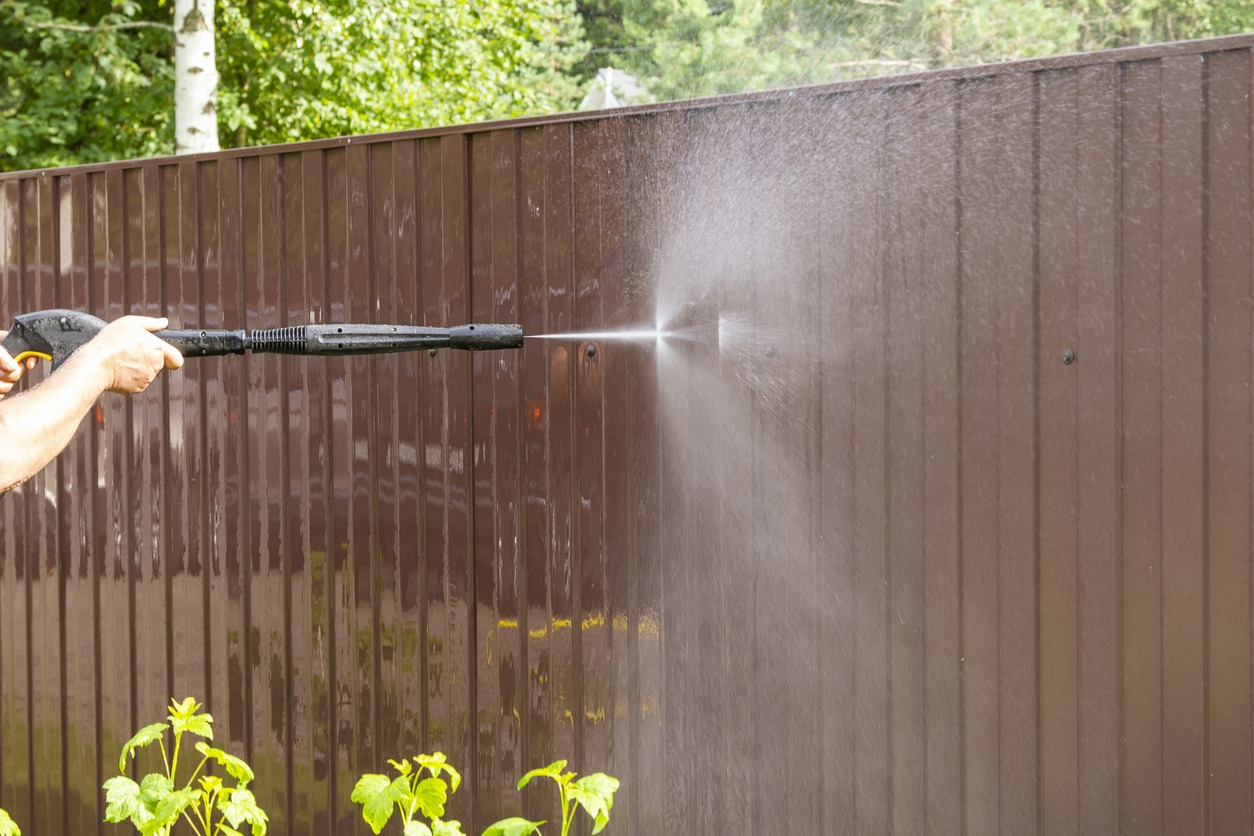 Cleaning fence with high pressure power washer, cleaning dirty wall.