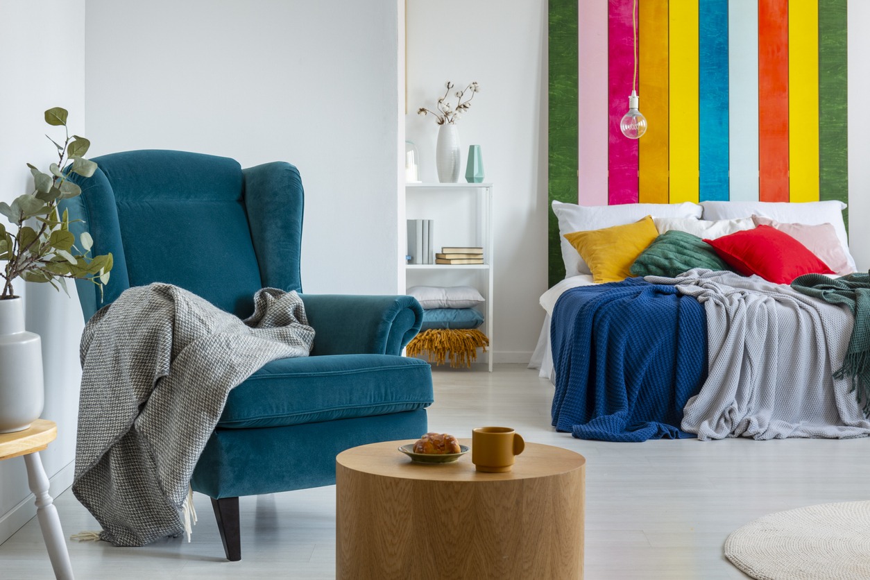 Coffee and peace of cake next to wing back chair with grey blanket in warm bedroom interior