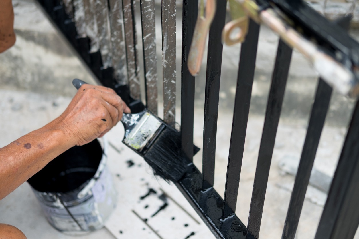 Hand with paintbrush painting iron fence with black paint. Concept of renovation house