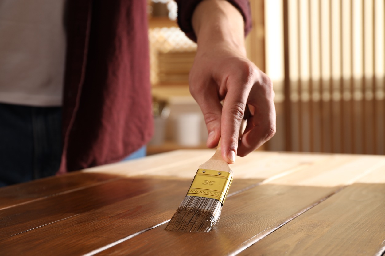 Man with brush applying wood stain onto wooden surface indoors, closeup