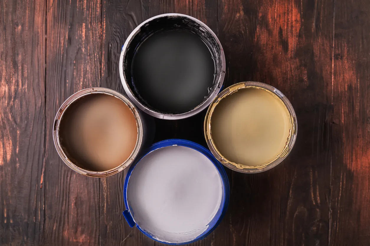 Open cans with white,black,brown and yellow paint on wooden background, top view