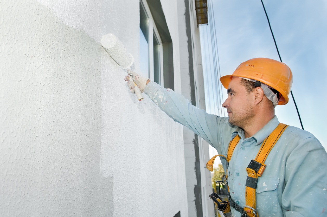 A builder painting a wall while wearing safety gear