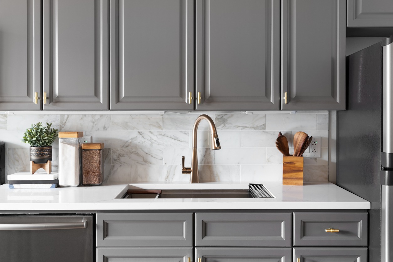 A gold kitchen faucet detail with grey cabinets