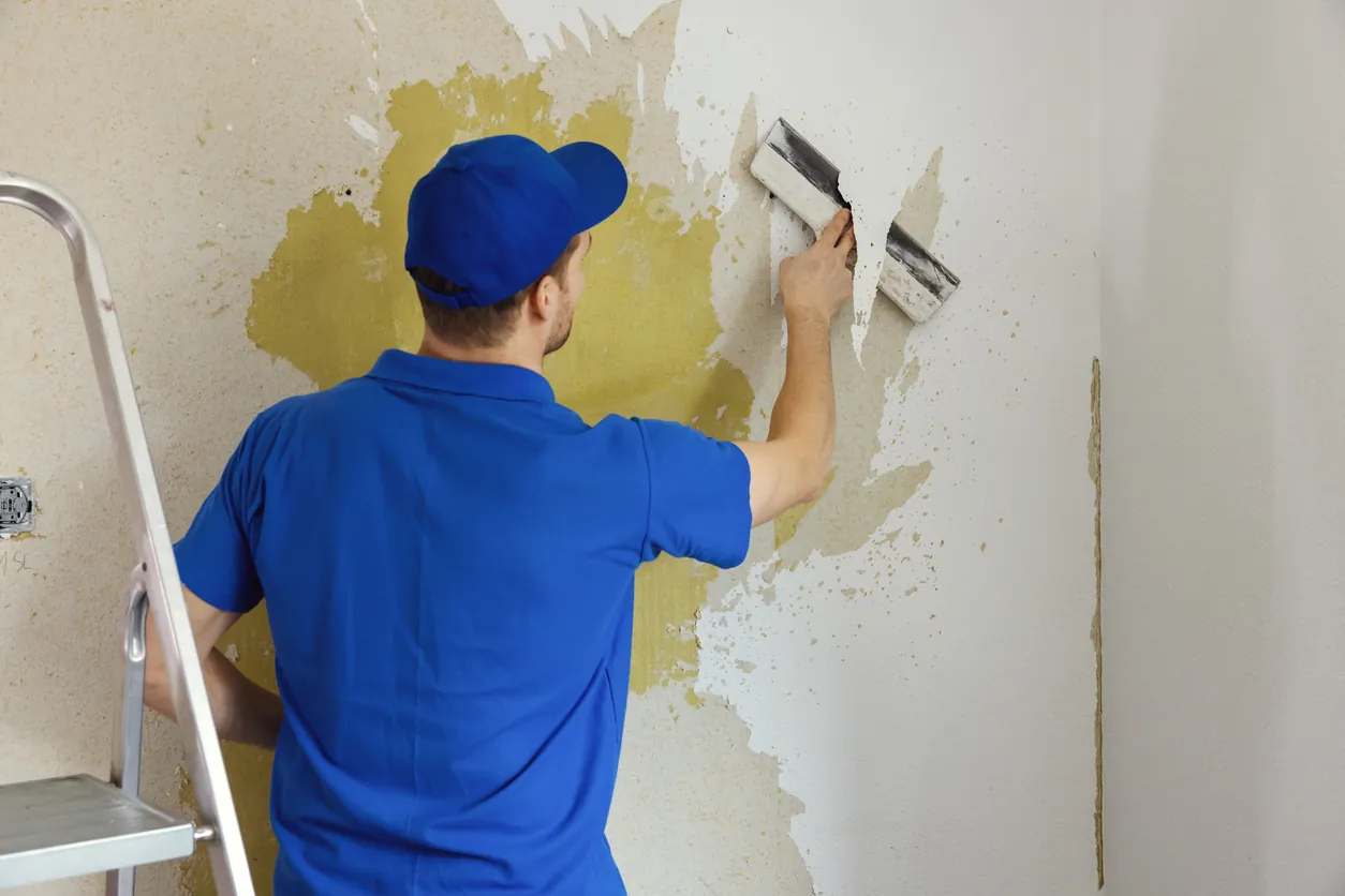 worker removing old painted wallpaper from the wall. house renovation interior renewal