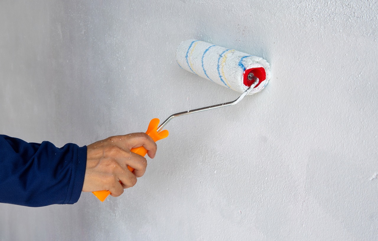 A close-up photo of hand painting a blank white wall with a paint roller.