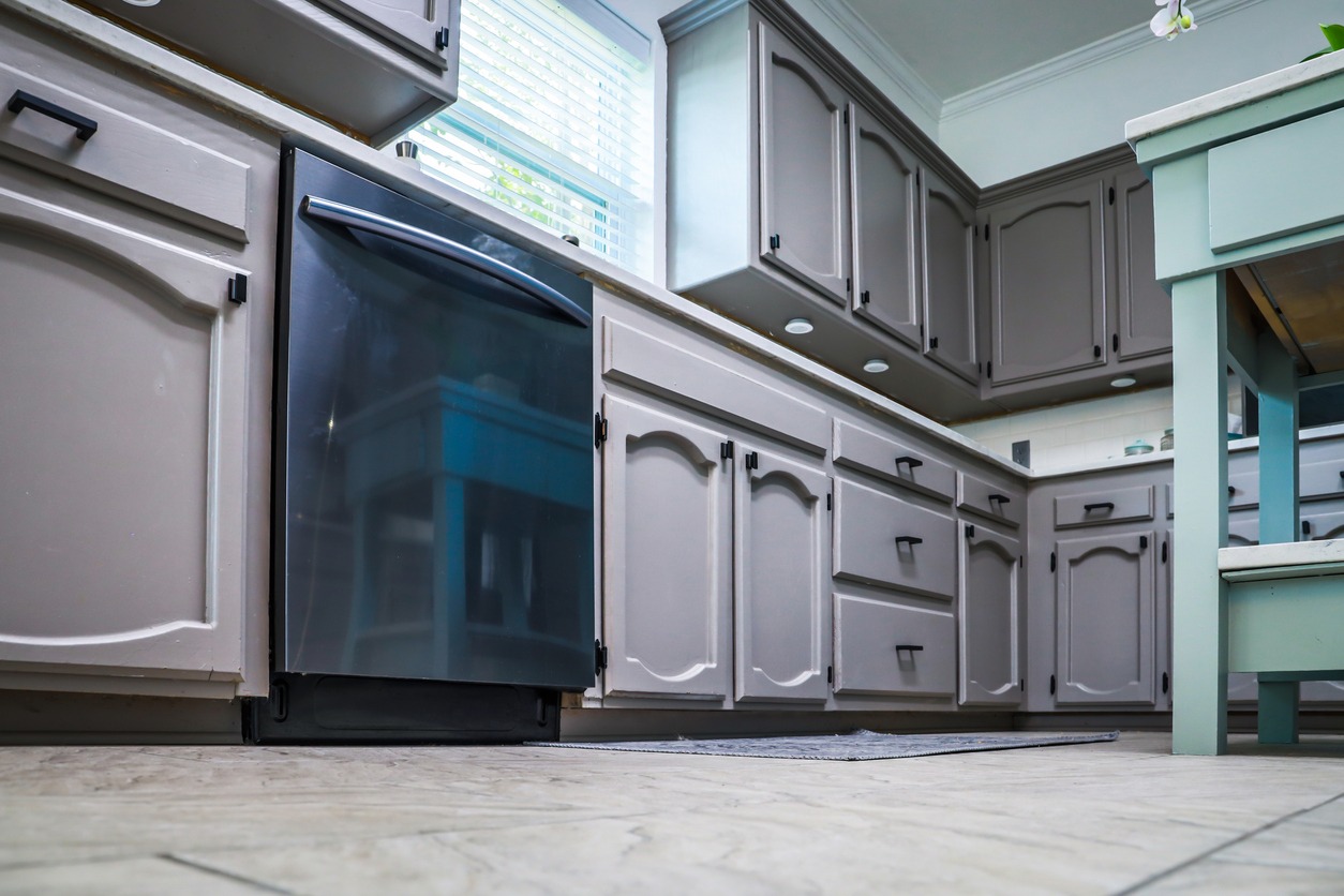 Low angle view of a renovated kitchen in an older home with painted gray cabinets, marble countertops, a small portable island and a tiled floor