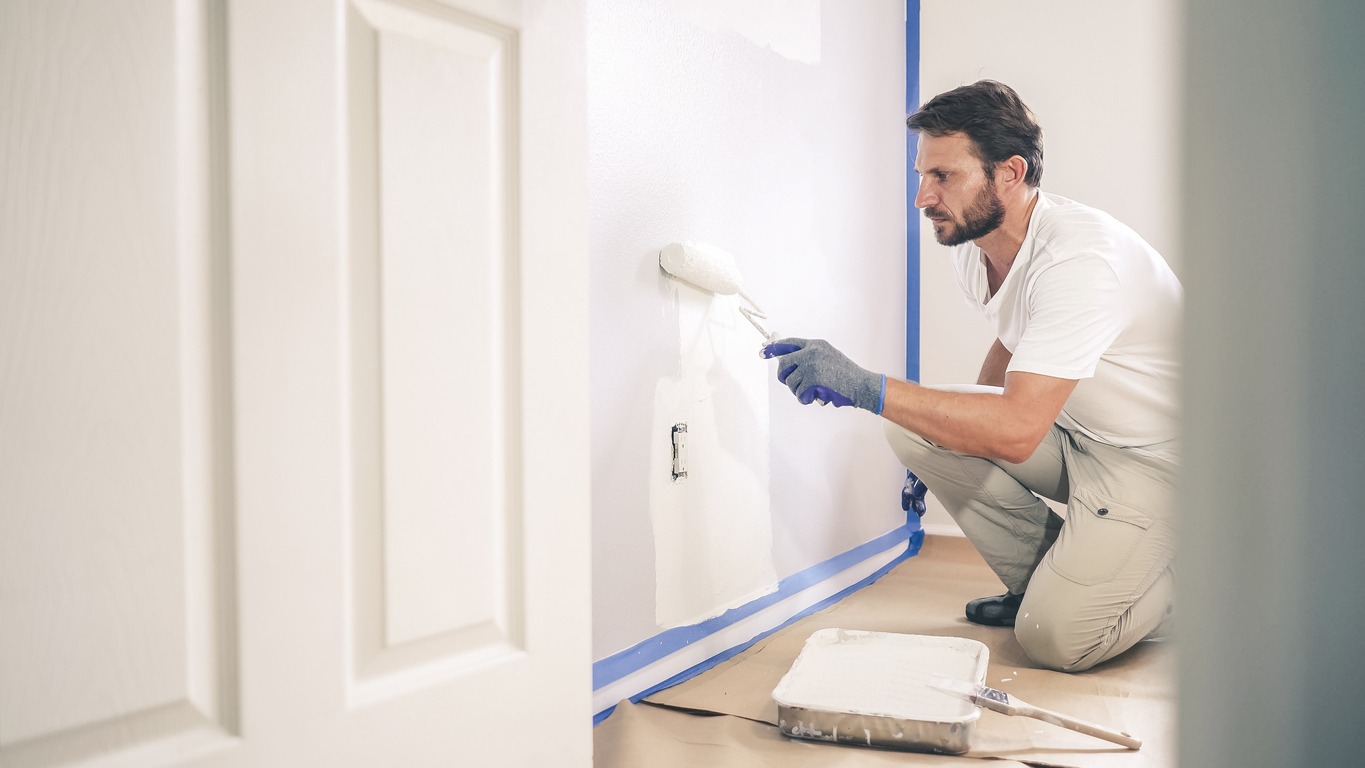 Painter man painting the wall in home, with paint roller and white color paint. Room renovations at house.