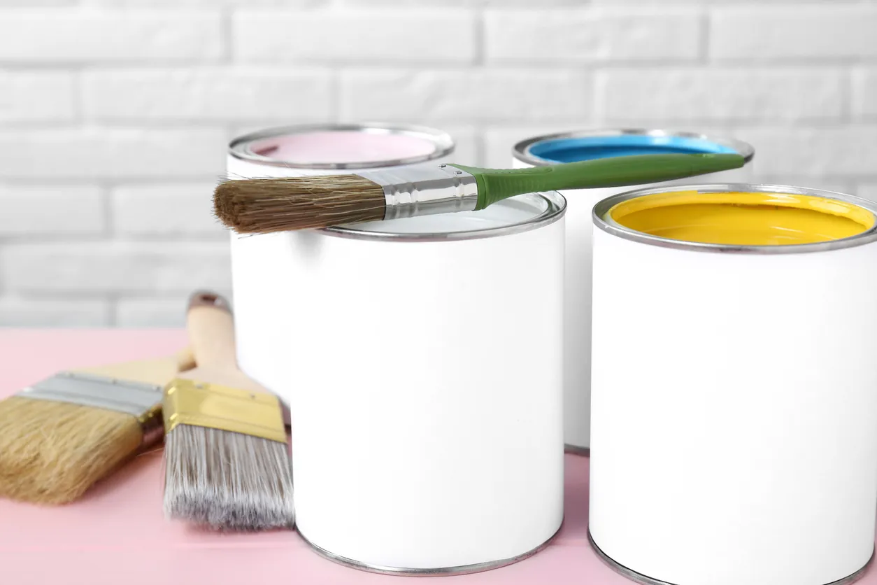 Cans of colorful paints and brushes on pink table, closeup